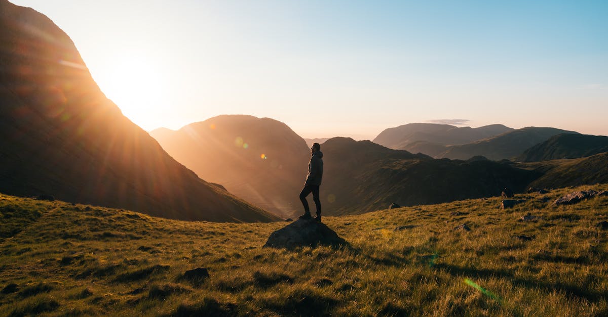 Silhouette of a person standing on a hill during sunrise in Cumbria, England with scenic mountain views.