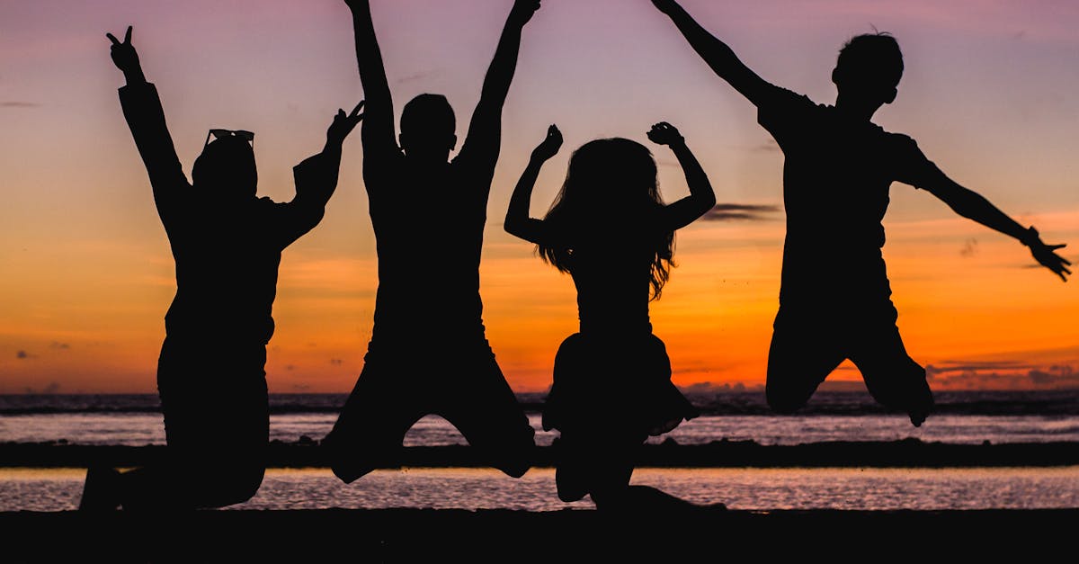Silhouette of friends jumping on the beach at sunset, celebrating summer fun.